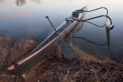 4367620-long-and-slim-racing-outrigger-canoe-black-carbon-fiber-design-with-a-paddle-on-shore-of-calm-lake.jpg